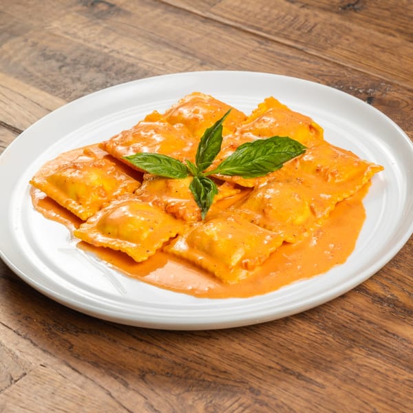 Tutto Pizza & Pasta's ravioli in a creamy orange sauce, garnished with fresh basil on a white plate.