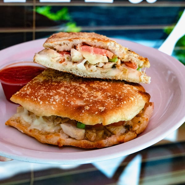 A chicken panini with melted cheese, tomatoes, and green peppers, served with a side of marinara sauce.