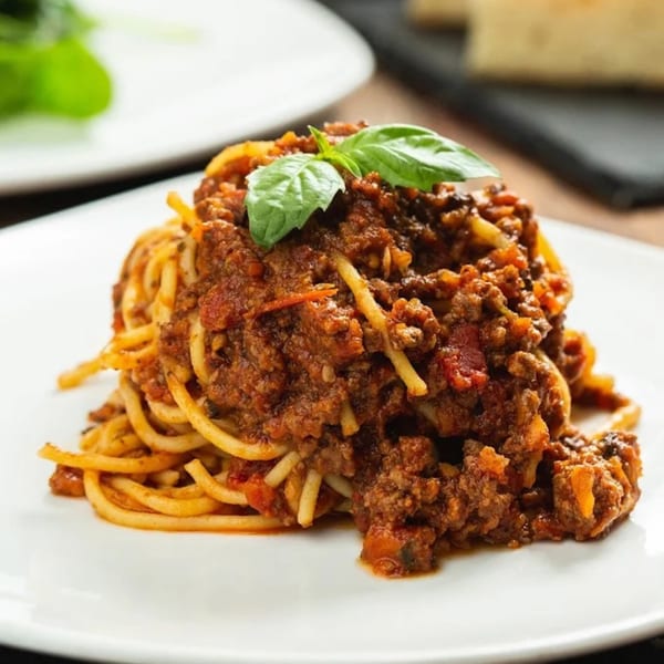 Spaghetti bolognese with rich meat sauce and fresh basil on a white plate.