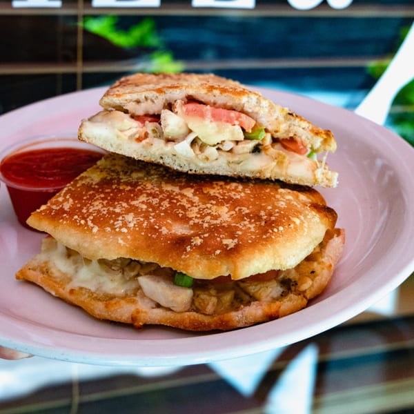 A calzone, sliced in half, revealing chicken, cheese, and vegetables, with a side of marinara.