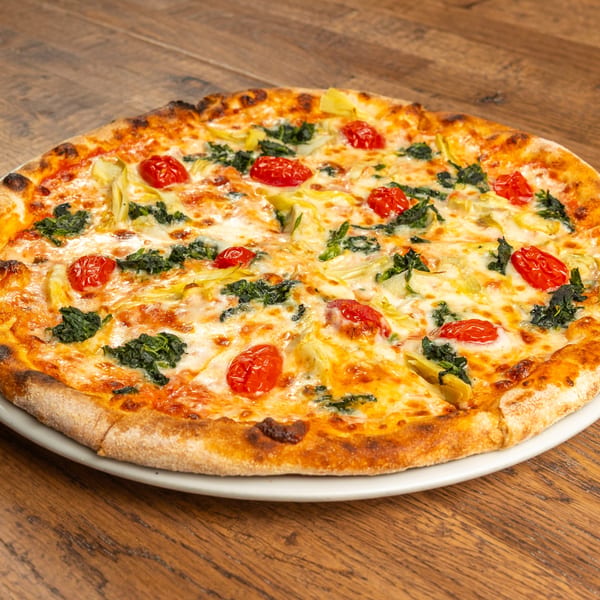 Tutto Pizza & Pasta's pizza with spinach, artichoke hearts, and cherry tomatoes on a wooden table.