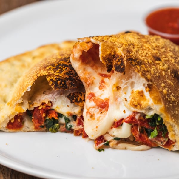 A Tutto Pizza & Pasta calzone, cut open to reveal melted cheese, sun-dried tomatoes, and spinach.