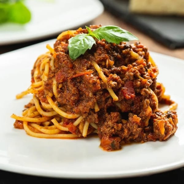 Spaghetti bolognese with rich meat sauce and fresh basil on a white plate at Tutto Pizza & Pasta.