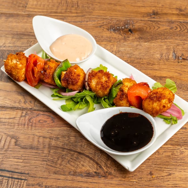 Crispy fried chicken and vegetable skewers with two dipping sauces on a white plate.
