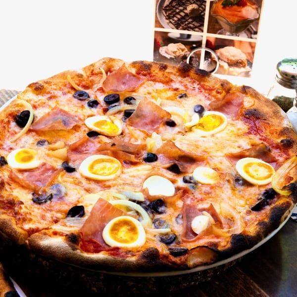 A Tutto Pizza & Pasta pizza with ham, olives, onions, and sliced hard-boiled eggs.