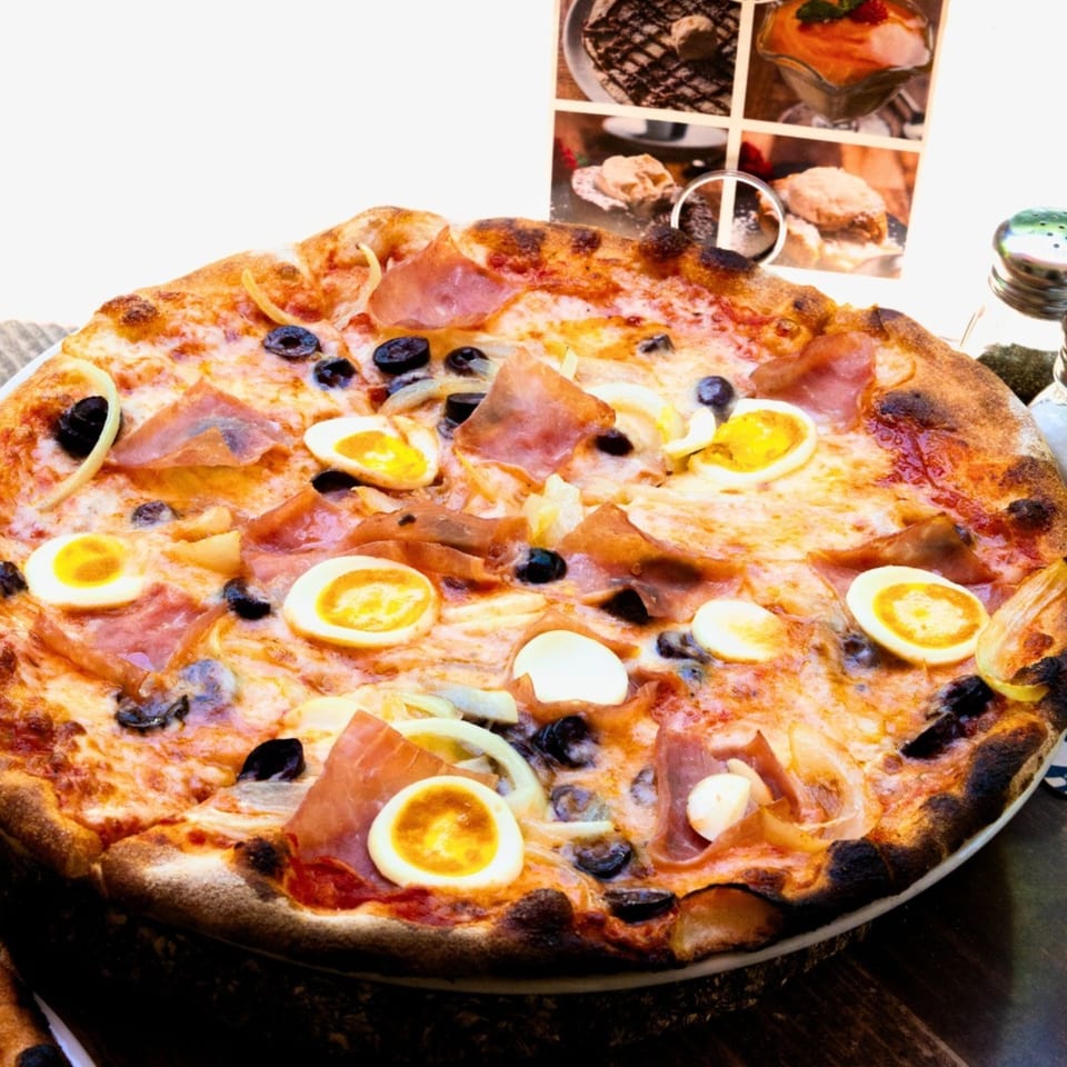 A Tutto Pizza & Pasta pizza with ham, olives, onions, and sliced hard-boiled eggs.