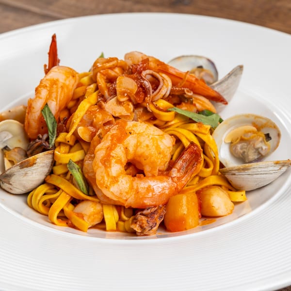 Seafood pasta with shrimp, clams, and calamari in a red sauce on a white plate.