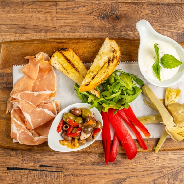 Tutto Pizza & Pasta antipasto board with prosciutto, grilled bread, olives, peppers, artichokes, and burrata.