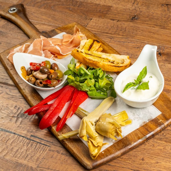 Tutto Pizza & Pasta's antipasto board with prosciutto, grilled bread, olives, peppers, artichokes, and burrata.