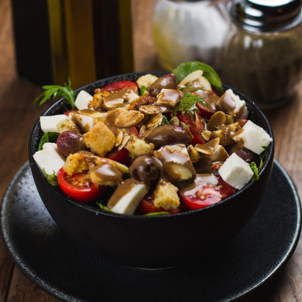 A vibrant salad with cherry tomatoes, feta, olives, croutons, and dressing in a black bowl.