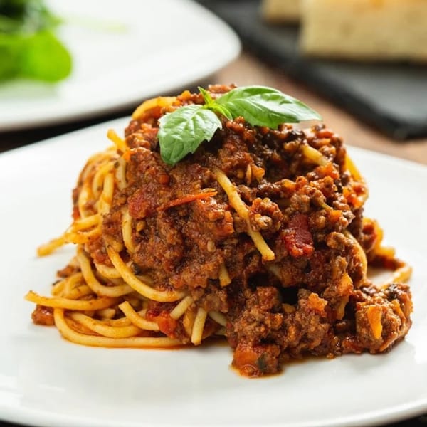Spaghetti Bolognese from Tutto Pizza & Pasta, topped with fresh basil on a white plate.